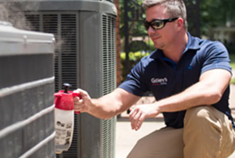 A Gilley's technician in a navy Gilley's shirt sprays cleaner on an outdoor coil