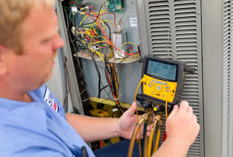 A Gilley's technician reads a gauge set connected to an outdoor unit's service panel
